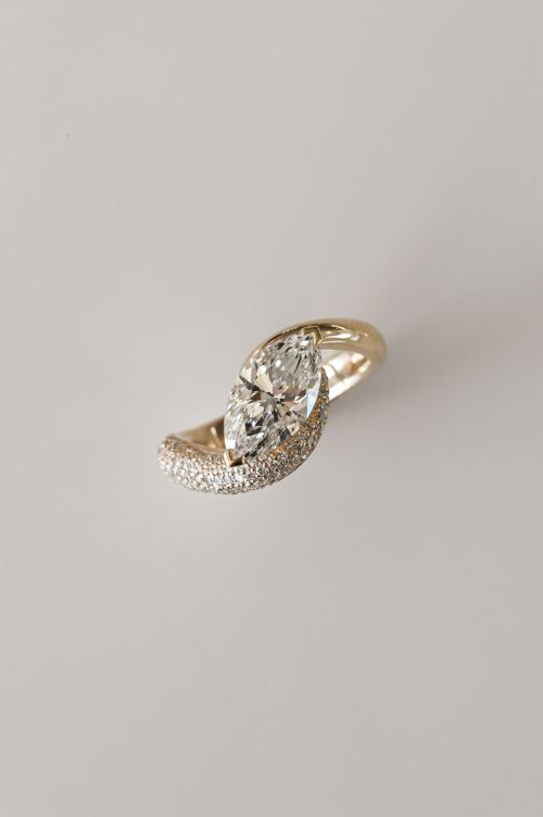 Aria engagement ring in 14k yellow gold, top view featuring a marquise-cut diamond nestled between asymmetrical curved bands—one sleek, one pavé-set—creating a sculptural, entwined silhouette.