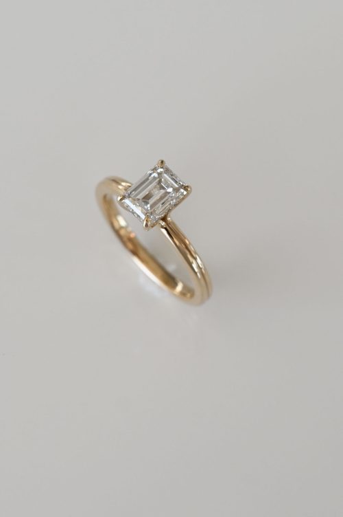 Chloe engagement ring in 14k yellow gold with 14k ultra white gold setting, angled view showcasing the emerald-cut diamond with hidden halo detail.