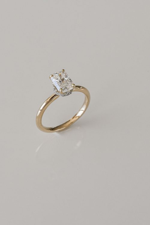 Ophelia engagement ring in 14k yellow gold with 19k white gold setting, angled view featuring an elongated cushion-cut diamond with hidden halo and surprise diamond accents.