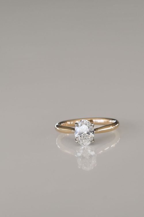 Zoe engagement ring in 14k yellow gold with 14k ultra white gold setting, front view showcasing the oval-cut diamond held in a criss-cross head design.