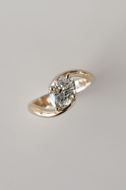 Selene engagement ring in 14k yellow gold, top view featuring an oval diamond delicately cradled between two curved, polished gold arms in a seamless and balanced design.