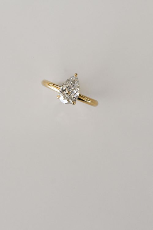 Iris engagement ring in 18k yellow gold, featuring a pear-cut diamond with petal-style prongs and a hidden halo accent.