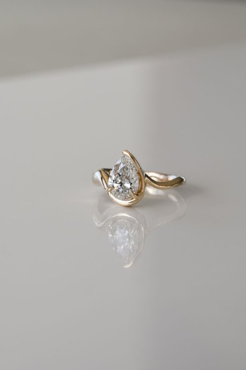 Amara engagement ring in 14k yellow gold, front view featuring a pear-shaped diamond cradled by two sculptural gold arms in a softly curved, asymmetrical design inspired by an intimate embrace.