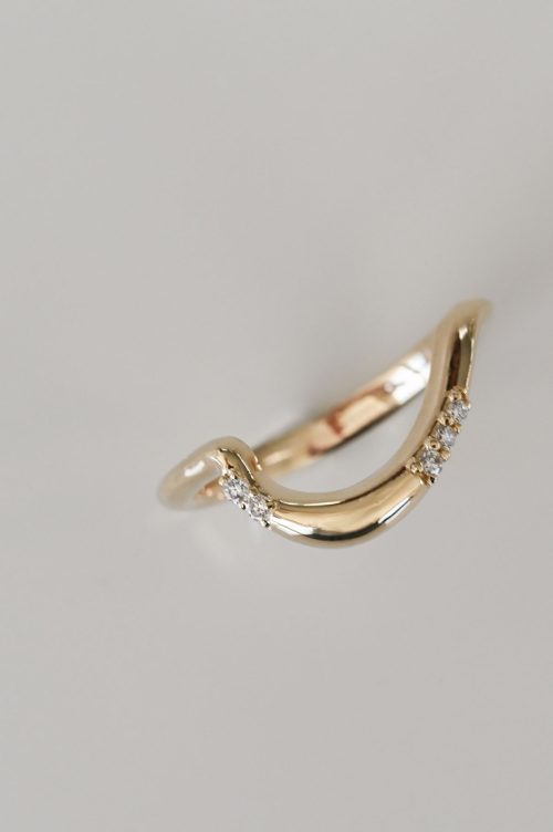 Mira wedding band in 14k yellow gold, top view featuring a soft, sculptural curve with scattered pavé diamonds designed to nestle seamlessly beside the Mira engagement ring.
