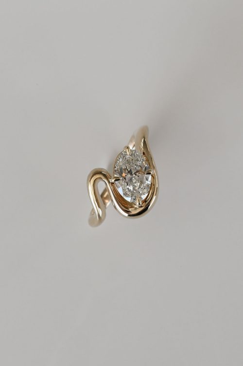 Mira engagement ring in 14k yellow gold, top view featuring an oval diamond nestled within a fluid, sculptural band that curves in an open, asymmetrical embrace.