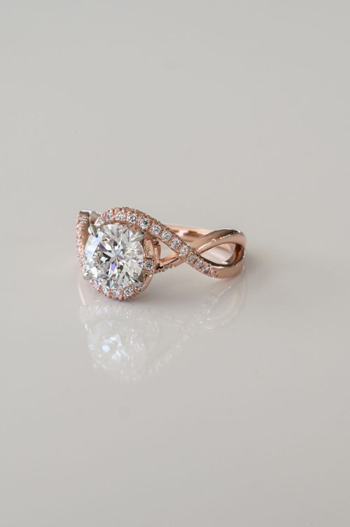Angelica engagement ring in 14k rose gold with 19k white gold setting, front view featuring a round brilliant diamond wrapped in a pavé infinity twist band.