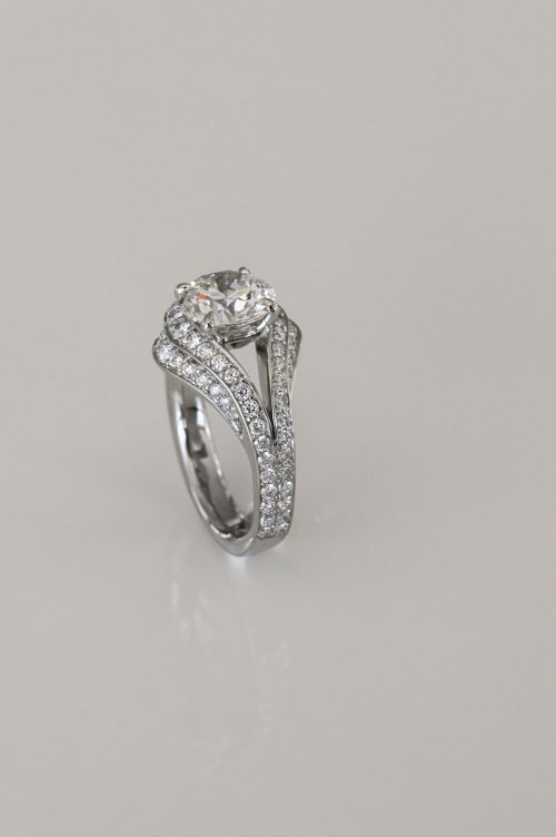Sonja engagement ring in 19k white gold, angled view featuring a round brilliant diamond set in a split-shank design with pavé diamonds wrapping around the flowing band.