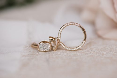 Eloise engagement ring in 14k yellow gold with a bezel-set cushion-cut diamond, shown beside the Eleanor engagement ring featuring an oval-cut diamond in a sculpted knot setting with pavé diamonds lining the band and interior.