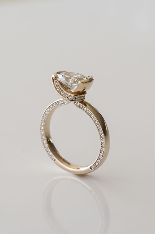 Eleanor engagement ring in 14k yellow gold, side profile view featuring an oval-cut diamond held in a sculpted knot setting with pavé diamonds lining the inner shank.