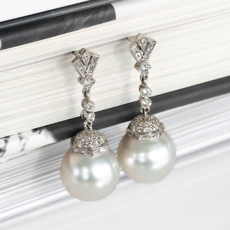 Art Deco drop earrings featuring white South Sea pearls, pavé diamond caps, and geometric diamond-set motifs in platinum.