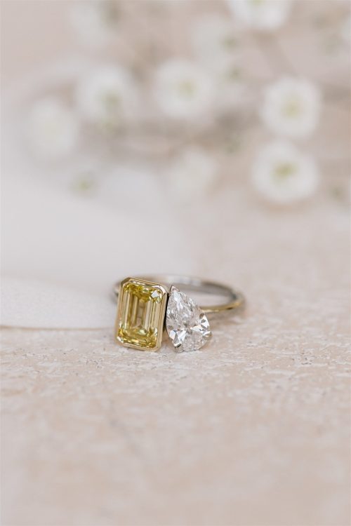 Close-up of the Ava ring featuring a yellow emerald-cut diamond and a white pear-cut diamond set side by side on a polished band.