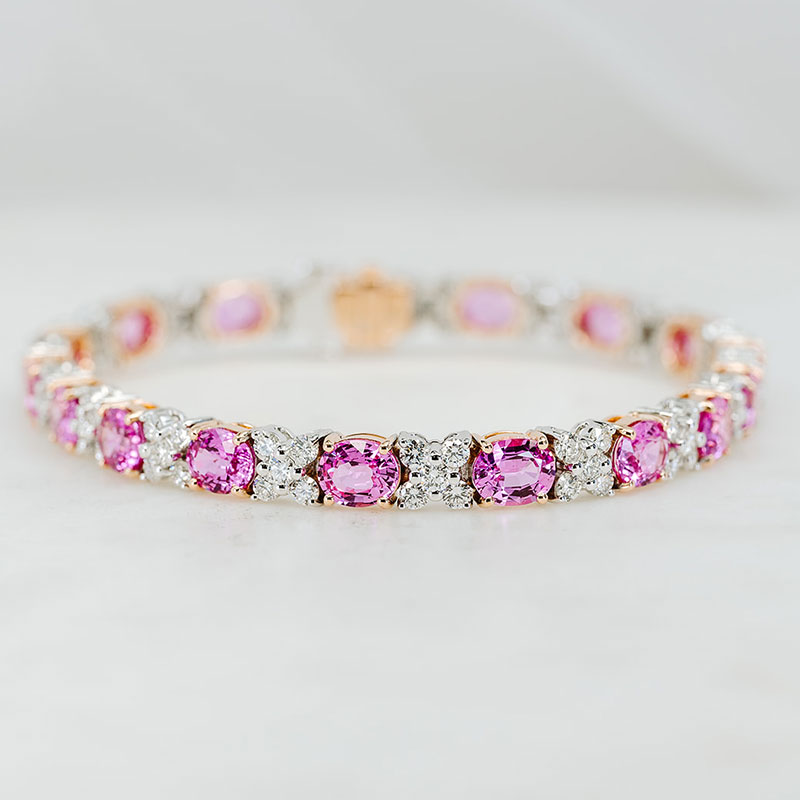 White and rose gold bracelet featuring alternating oval pink sapphires and round diamond clusters.