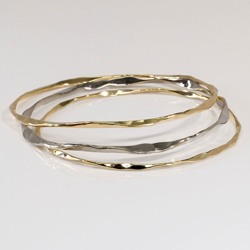 Set of three hammered bangles in mixed metals, featuring both yellow gold and white gold finishes.