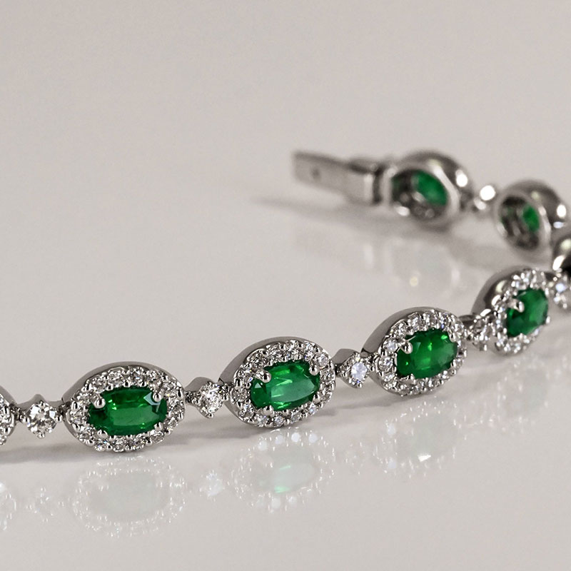 White gold bracelet featuring oval green emeralds framed by diamond halos and accented with round diamond links.