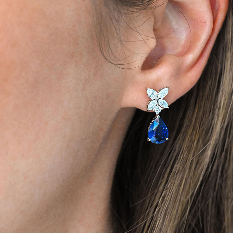 Drop earrings featuring pear-shaped blue gemstones suspended from white gold floral studs with pavé diamond petals.