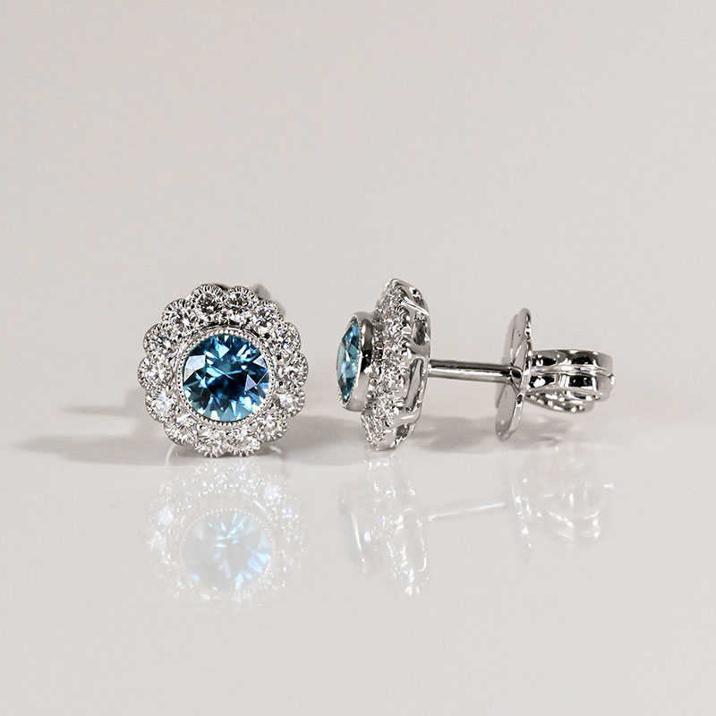 White gold earrings featuring round blue center stones surrounded by a scalloped double halo of pavé-set white diamonds.