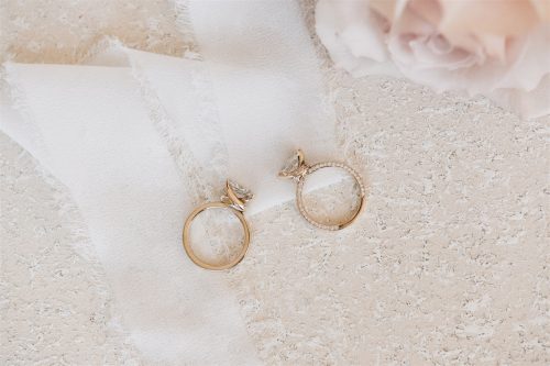 Overhead view of the Eleanor and Eloise rings styled on soft ivory fabric—Eleanor features a marquise diamond with tapered baguette side stones on a polished gold band, while Eloise showcases a marquise center stone with a pavé diamond band and hidden halo detail.