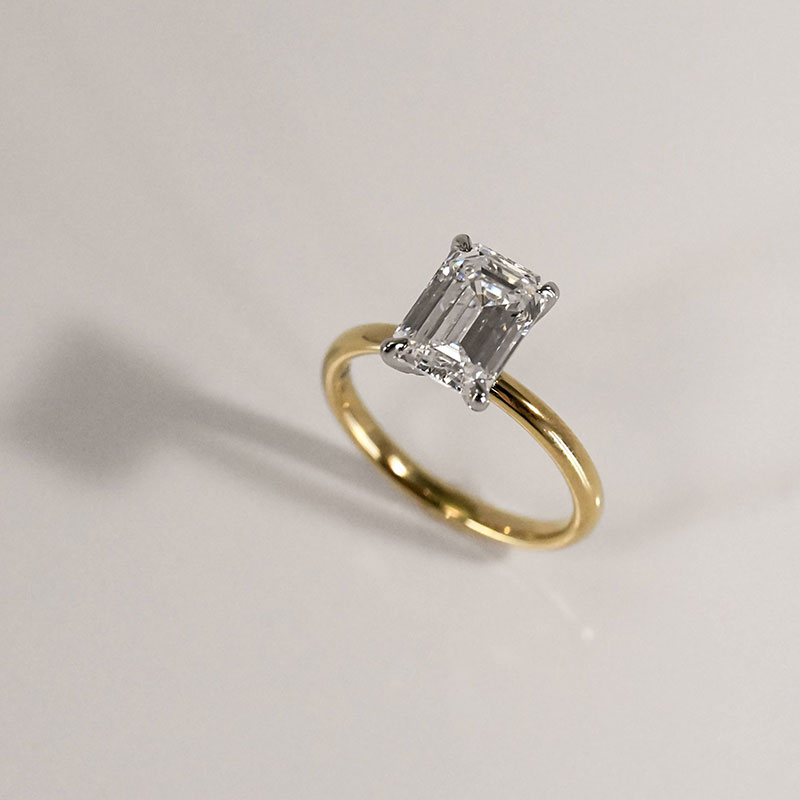 Emerald-cut diamond solitaire engagement ring with a white gold setting and yellow gold band.