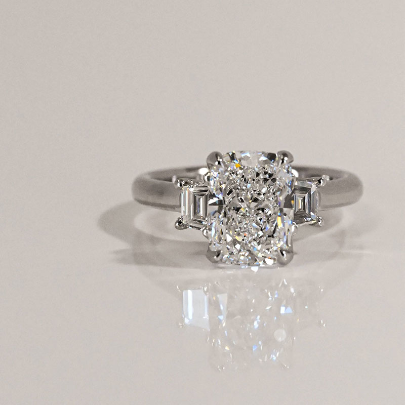 Three-stone engagement ring in platinum featuring a cushion-cut center diamond flanked by two baguette-cut side diamonds.