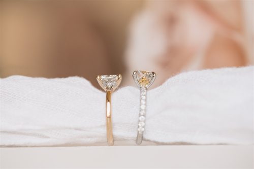 Side profile view of the Flora and Florence rings resting on soft white fabric, showcasing their delicate gallery details—Flora with a diamond-set leaf motif and Florence with a golden floral cluster beneath the center stone.