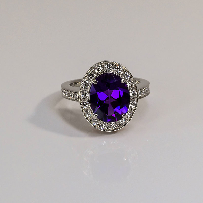 GemstoneRings-3 White gold ring with a large oval-cut purple gemstone surrounded by a halo of small round diamonds and diamond-accented band.