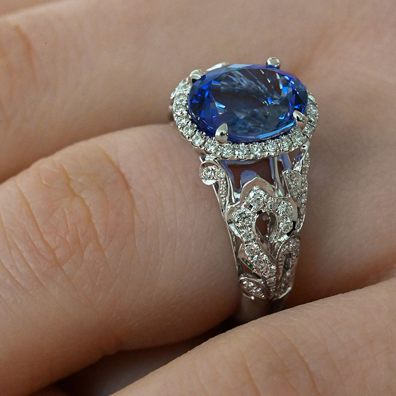 GemstoneRings-5 White gold ring featuring an oval blue sapphire center stone, surrounded by a diamond halo and intricate diamond-accented filigree band.