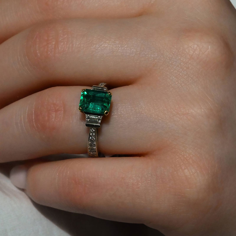 GemstoneRings-6 Emerald-cut green emerald ring with diamond side accents and a pavé diamond band, shown on hand.