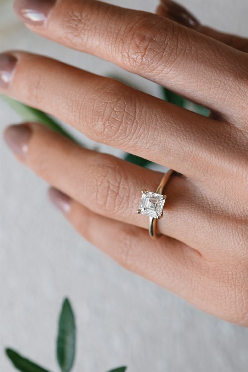 Close-up of the Harper engagement ring, featuring a square emerald-cut diamond set in a classic four-prong setting on a polished yellow gold band, worn on the hand for a refined and timeless look.