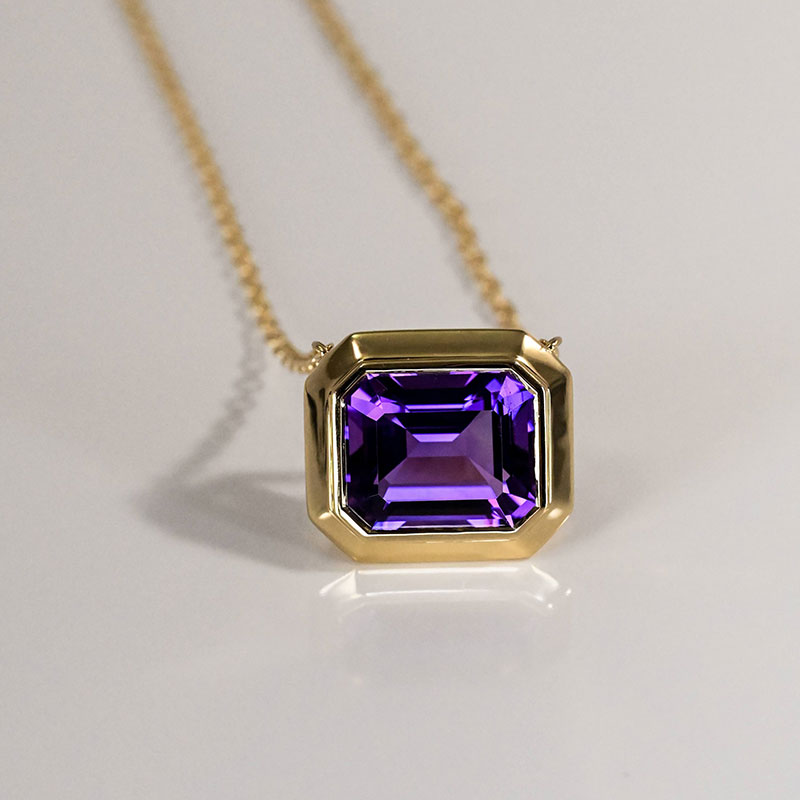 Yellow gold pendant necklace featuring an emerald-cut amethyst in a bold bezel setting.