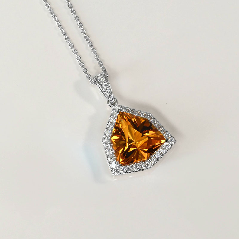 White gold pendant necklace featuring a vivid orange trillion-cut gemstone framed by a halo of small round diamonds.