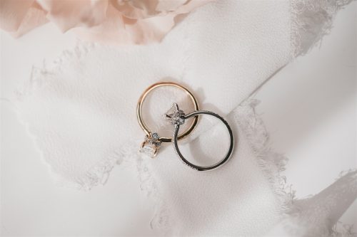 Overhead view of the Ophelia and Cecelia rings resting on soft ivory fabric—Ophelia features a yellow gold band with a radiant-cut diamond and hidden bezel detail, while Cecelia showcases a platinum band with pavé accents and a radiant-cut diamond.
