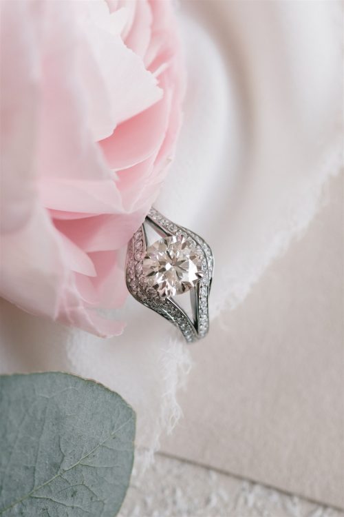 Close-up of the Sonja ring nestled against a soft pink peony—featuring a brilliant round-cut center diamond framed by tapered baguette side stones and pavé diamond detailing that sweeps elegantly along a split-shank platinum band.