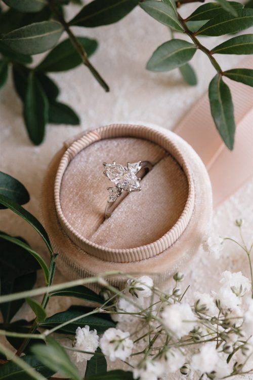 The Violet ring set in a blush velvet box, featuring a marquise diamond flanked by two kite-shaped side stones, surrounded by delicate florals and soft greenery.