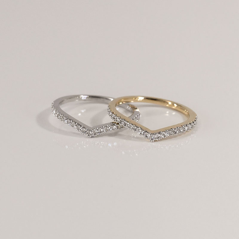 Chevron-shaped wedding bands in white and yellow gold, each set with a row of pavé diamonds along the top curve.