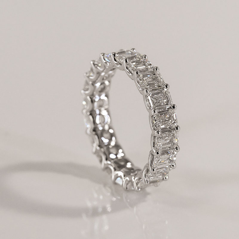Platinum eternity band set with rectangular emerald-cut diamonds in a continuous prong setting.