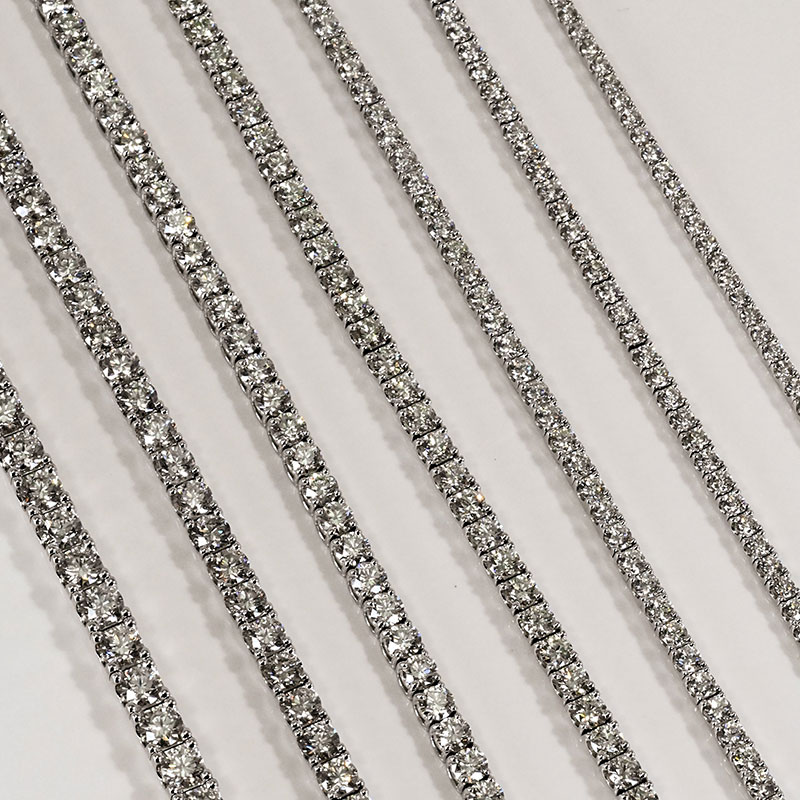 Close-up of multiple diamond tennis bracelets arranged diagonally on a white surface.