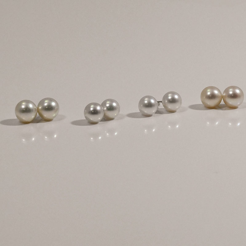 Four pairs of round pearl stud earrings in varying shades of white, cream, and silver on a neutral background.