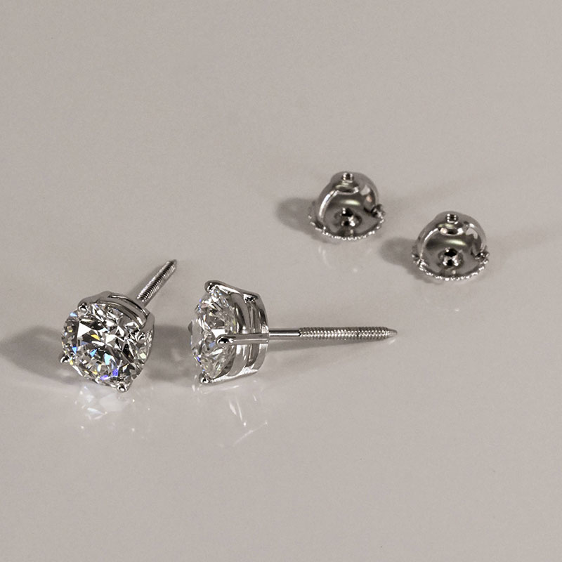 Round diamond stud earrings with screw back posts and matching earring backs on a neutral surface.