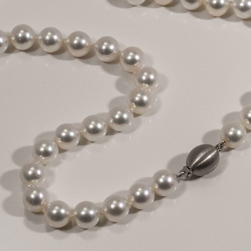 Close-up of a white pearl necklace with a matte silver ball clasp on a neutral background.