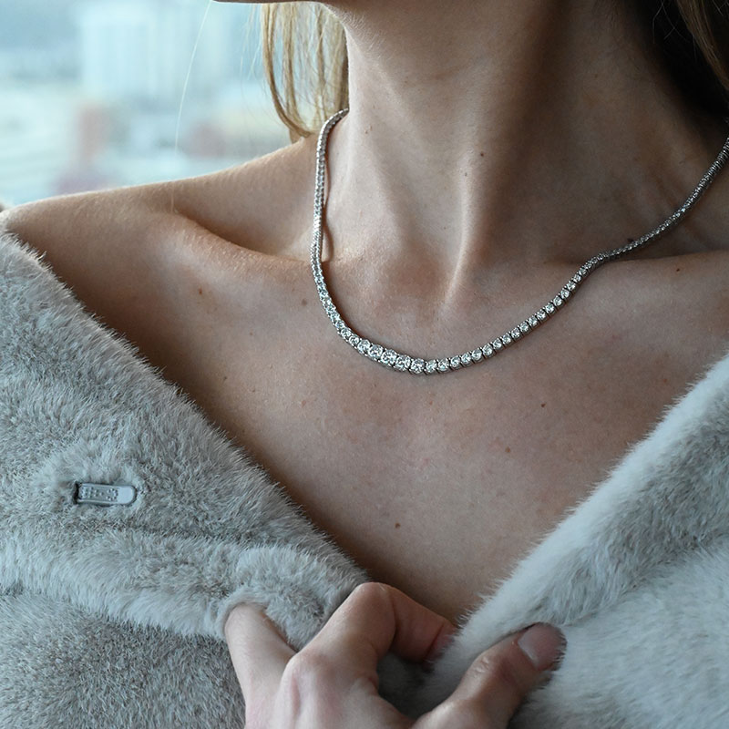 Woman wearing a graduated diamond tennis necklace with round-cut stones and a fur wrap.